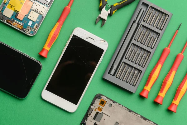 Damaged mobile phones with technician tools on color background