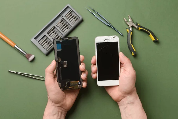 Male technician with disassembled mobile phone and technician tools on color background