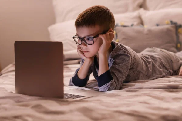 Cute boy watching cartoons in bedroom at night