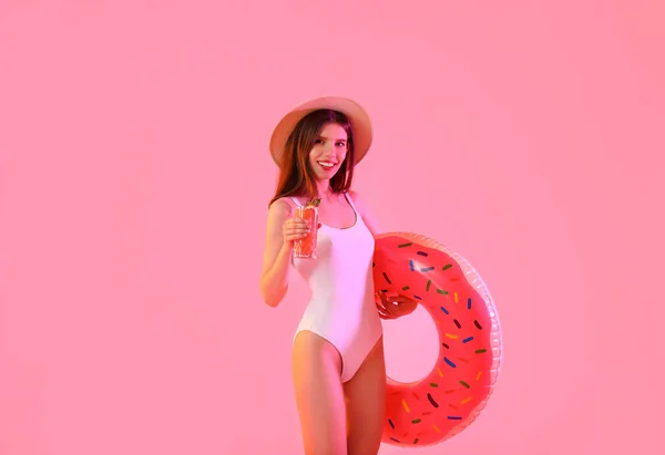 Beautiful young woman with cocktail and swimming ring on color background