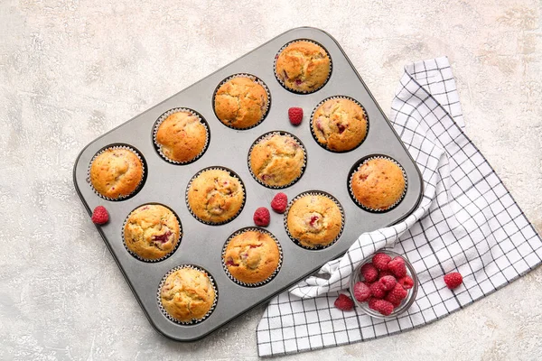 Baking tin with tasty raspberry muffins on light background