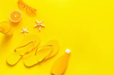 Arka planda parmak arası terlik, güneş gözlüğü, güneş kremi ve bir bardak meyve suyu olan kompozisyon