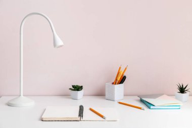 Renk duvarının yanındaki masada kırtasiye malzemesi olan modern lamba.