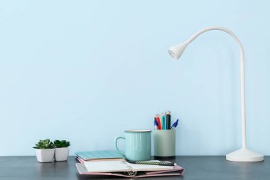 Renk duvarının yanındaki masada kırtasiye malzemesi olan modern lamba.