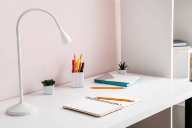 Renk duvarının yanındaki masada kırtasiye malzemesi olan modern lamba.