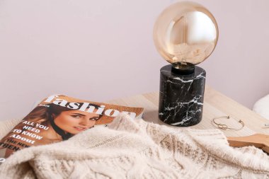 Renkli duvarın yanındaki masa üzerinde dergi ve giysileri olan şık bir lamba.