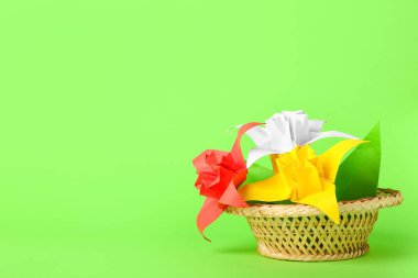 Basket with origami daffodils on color background