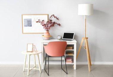 Vazo ve çiçek açan dallarla aydınlık duvarın yanında şık bir iş yeri.