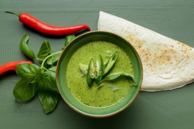 Bir kase lezzetli yeşil körili tavuk ve ahşap arka planda malzemeler.