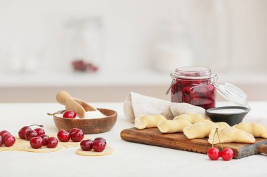 Mutfaktaki masada çiğ kirazlı hamur tatlısı ve malzemelerle ahşap tahta.
