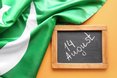Renk arkaplanında Bağımsızlık Günü tarihi yazılı Pakistan bayrağı ve kara tahta