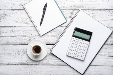 Bir fincan kahve, defterler, hesap makinesi ve tahta arka planda bir kalem.