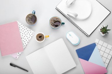 Kahve fincanları, bilgisayar faresi, kulaklık ve gri arkaplan üzerine not defterleri.