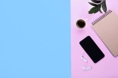 Bir fincan kahve, cep telefonu, kulaklık ve renkli arkaplan üzerine not defteri.