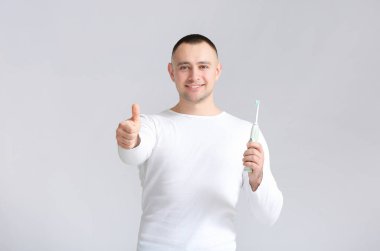 Diş fırçalı bir adam gri arka planda baş parmak gösteriyor.
