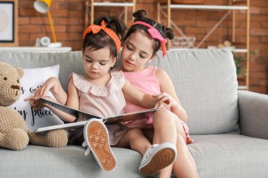 Evde kitap okuyan şirin küçük kız kardeşler.