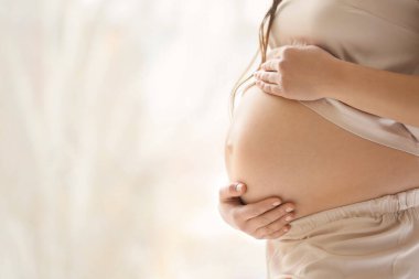 Evde pencerenin yanında hamile bir kadın var.