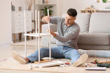 Genç adam evde mobilya montajı yapıyor.