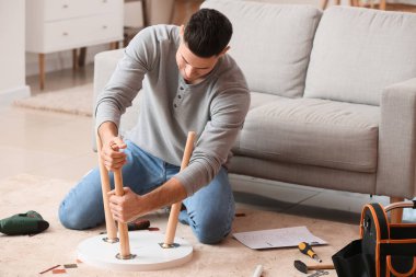 Genç adam evde mobilya montajı yapıyor.