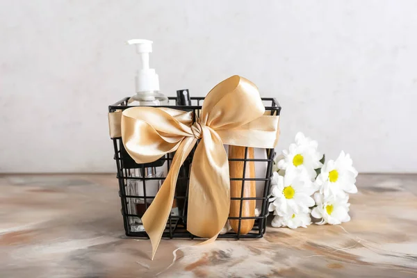 Gift basket with cosmetics and flowers on table