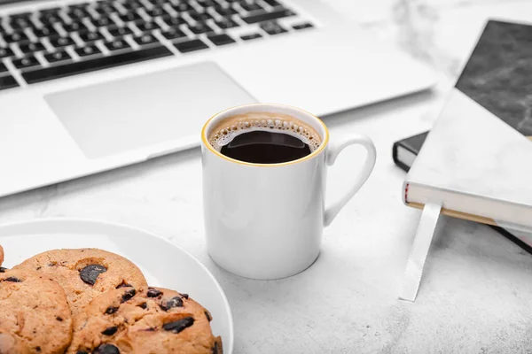 Cup of coffee, laptop, notebooks and tasty cookies on light background