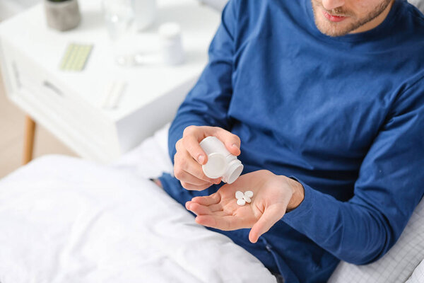 Красивый молодой человек, принимающий таблетки в спальне