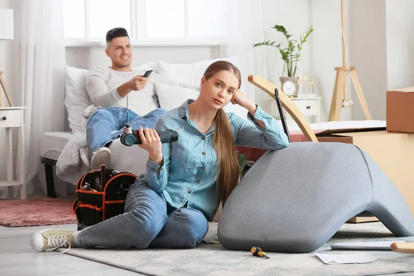 Young Woman Assembling Furniture While Her Lazy Husband Lying Bed — Stock Photo, Image