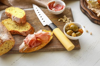 Hafif ahşap arka planda zeytinli ve jambonlu lezzetli bruschettalar hazırlanıyor.