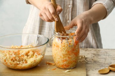 Woman putting tasty sauerkraut into glass jar on table in kitchen, closeup clipart