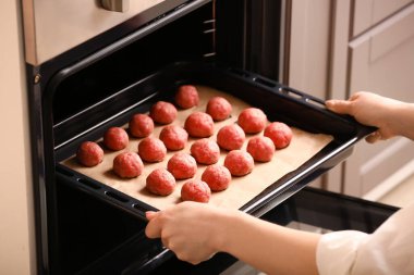 Kadın fırına taze etten yapılmış çiğ pirzola tepsisi koyuyor, yakın plan.