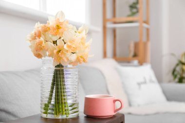 Güzel nergisli vazo ve odadaki koltukaltı masasında bir fincan çay.