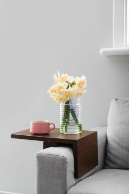 Güzel nergisli vazo ve odadaki koltukaltı masasında bir fincan çay.