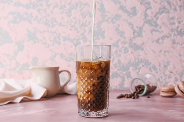 Arka planda sıcak kahve ve bardağa süt dökülüyor.