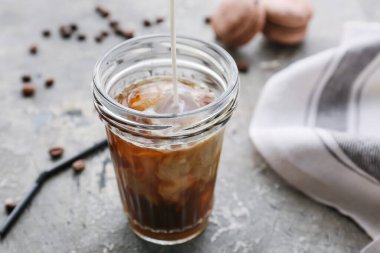 Süt bardağa dökülüyor. Arkaplanda sıcak kahve var.