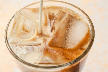 Hafif arka planda buzla kaplı sıcak kahve bardağına süt dökülüyor.