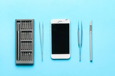 Renk arkaplanında teknisyen araçları olan hasarlı cep telefonu