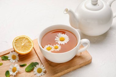 Bir fincan papatya çayı ve hafif arkaplanda çaydanlık ile kompozisyon