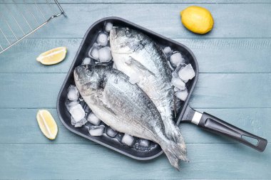 Ahşap arka planda çiğ dorado balıklı kızartma tavası.