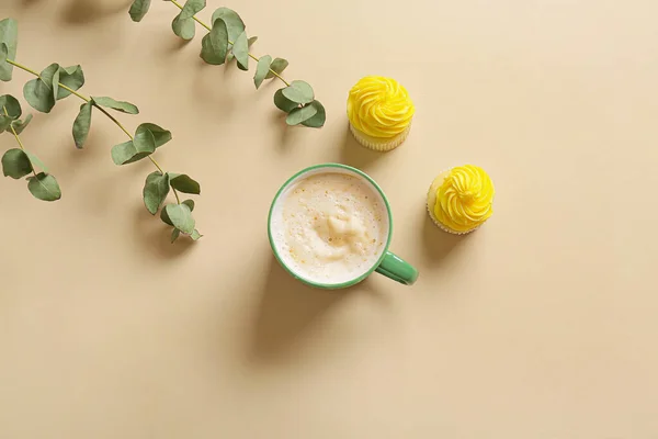 Cup of coffee with cupcakes and plant branches on color background