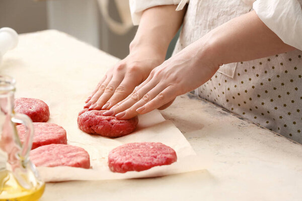 Woman preparing tasty cutlets made of fresh forcemeat at table in kitchen, closeup