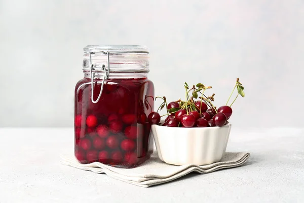 Glass jar with sweet cherry wine on light background