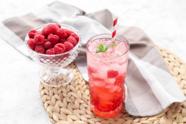 Bir bardak lezzetli limonata ve arka planda ahududulu kase.