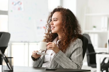 Ofisinde bir fincan kahve olan güzel genç bir kadın.