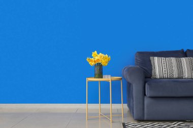 Odadaki kanepenin yanındaki masada narsist çiçekleri olan vazo.