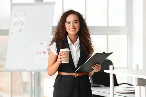 オフィスでコーヒーとクリップボードのカップを持つ美しい若い女性 — ストック写真