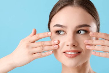 Güzel genç bir kadın yüzüne masaj yapıyor. Renkli arka planda, yakın plan.