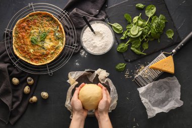 Kadın koyu arkaplanda ıspanaklı tart hazırlıyor.