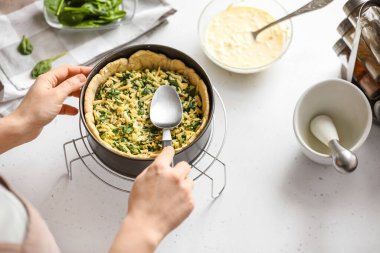 Kadın arka planda ıspanaklı tart pişiriyor.
