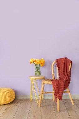 Masada güzel nergisli vazo ve renkli duvarın yanında ekoseli sandalye.