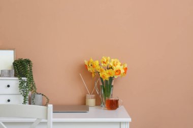 Dizüstü bilgisayarı ve renk arkaplanına karşı güzel nergisleri olan şık bir iş yeri